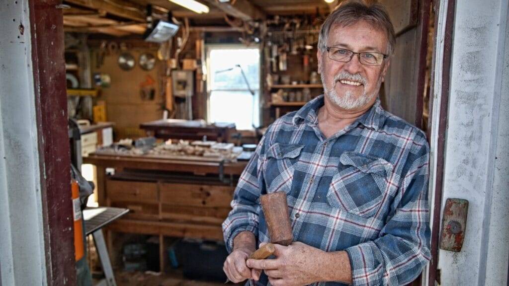 Artisan Lyon Serrurier 24/7 senior souriant avec un marteau dans les mains, représentant l'expérience dans l'artisanat de la serrurerie