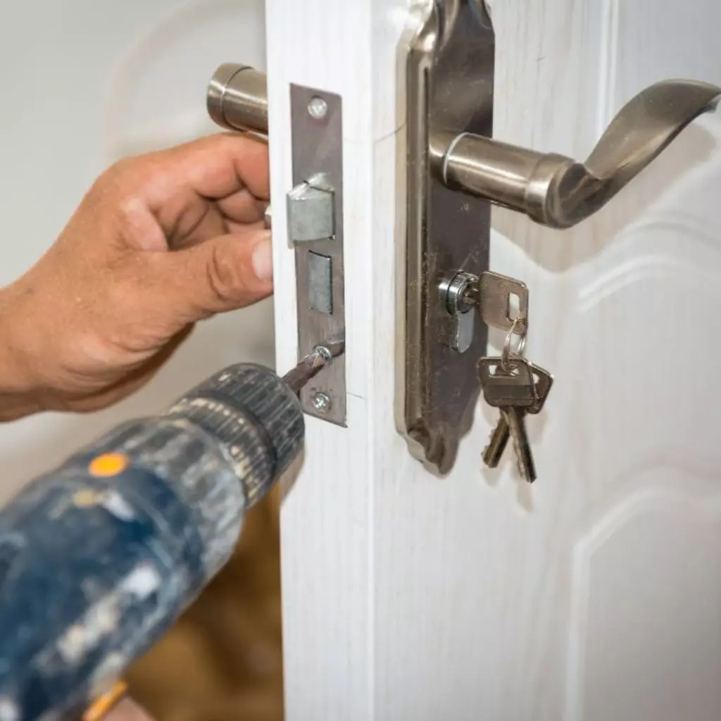 Serrurier Villeurbanne 3 Artisan serrurier utilisant une perceuse pour installer ou réparer une serrure sur une porte en bois avec une clé insérée.