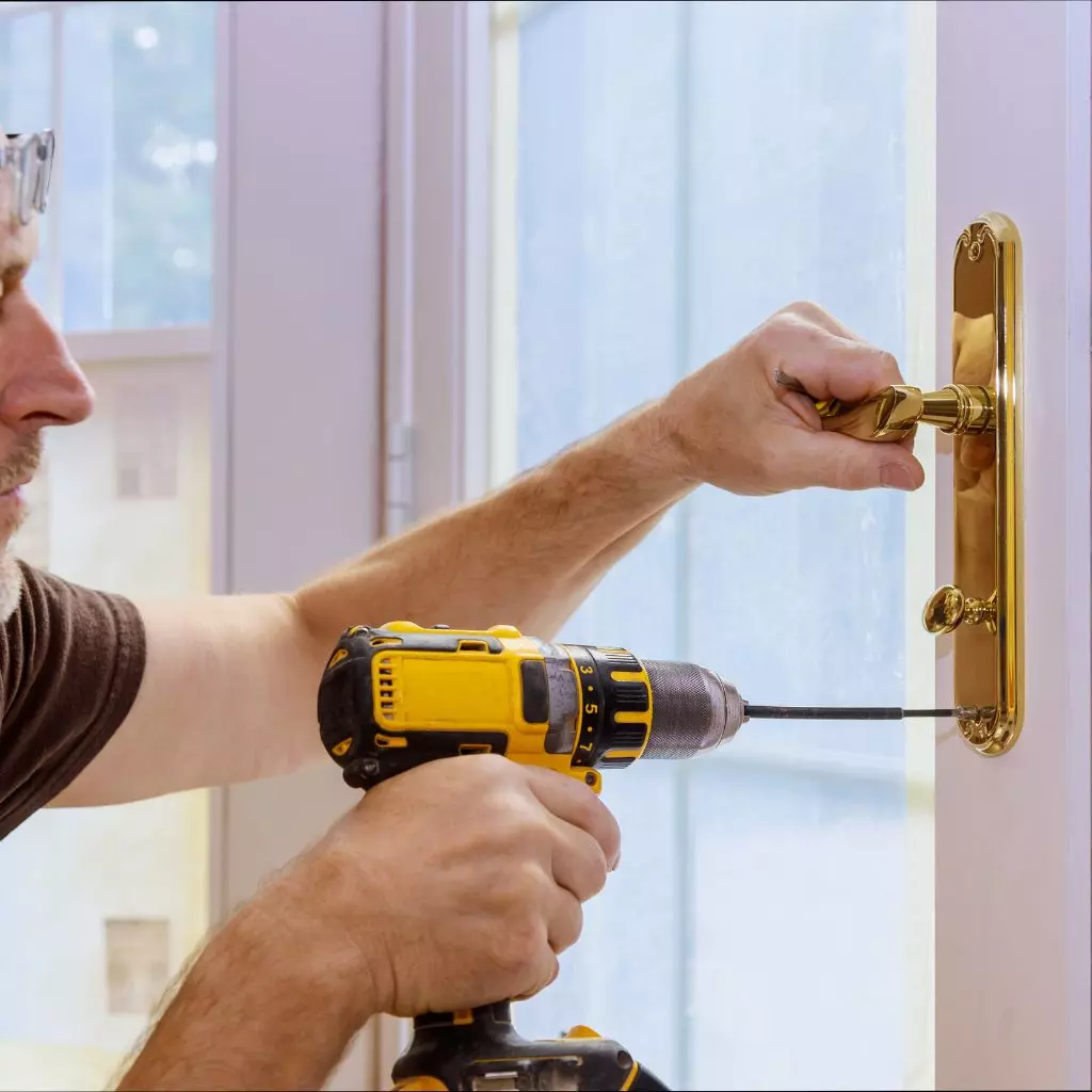 Serrurier Lyon 3 2 Serrurier utilisant une perceuse et un tournevis pour réparer une serrure dorée sur une porte vitrée.
